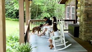 A porch with a stone wall, wooden railing, and a grassy area.