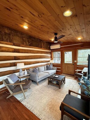 L’intérieur d’une cabane en rondins, avec un canapé, une table basse et un fauteuil.