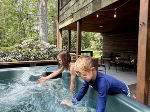 Un bain à remous où peuvent se détendre deux personnes, entouré d’une terrasse en bois et de verdure.