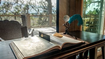 Une pièce avec une grande fenêtre, un bureau sur lequel est posé un livre ouvert, un globe terrestre et une plume d’oie.