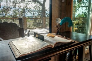 A room with a large window, a desk with an open book, a globe, and a feather quill.