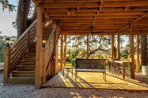 A wooden deck with a bench, a table, and a staircase leading to an upper level. - Unique Marshfront Treehouse Stay with Heated Soaking Tub & Adventure-Inspired Escape in Townsend, Georgia (Townsend)