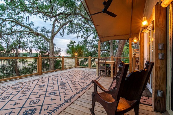 A covered outdoor deck with a patterned floor, wooden furniture, and a ceiling fan.