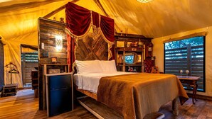 A tent-style room with a bed, a television, and a small table with glasses. - Unique Marshfront Treehouse Stay with Heated Soaking Tub & Adventure-Inspired Escape in Townsend, Georgia (Townsend)