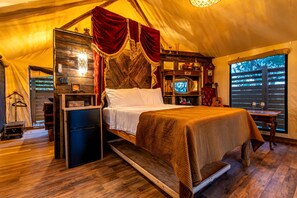 A tent-style room with a bed, a television, and a small table with glasses.