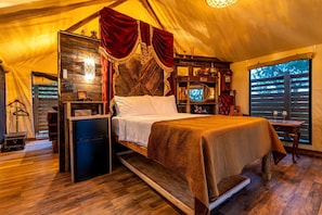A tent-style room with a bed, a television, and a small table with glasses.