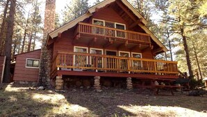 A log cabin with a balcony, stone chimney, and a deck. - Spacious Cabin with Large Porch Ideal for Groups in Arizona (Flagstaff)