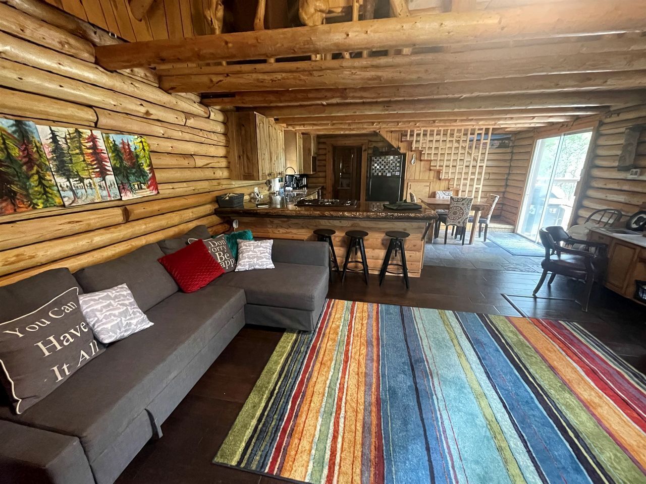 A log cabin interior with a sofa, striped rug, and a kitchen area.