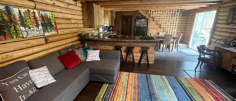 A log cabin interior with a sofa, striped rug, and a kitchen area.