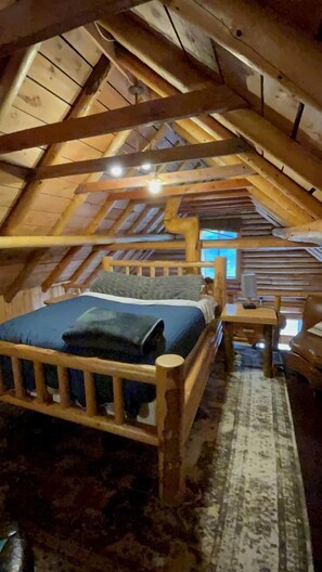 An attic bedroom with a wooden bed, a small table, and a window. - Relaxing Log Cabin Nestled in the Trees near Yellowstone, Idaho (Island Park)