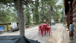 A wooden deck with red chairs and tables, surrounded by trees. - Relaxing Log Cabin Nestled in the Trees near Yellowstone, Idaho (Island Park)