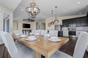 A modern dining room with a wooden table set for six, a chandelier, and a kitchen in the background. - New Listing!  In Morgantown w/ Pools, Tennis/Pickleball (Gulf Shores)