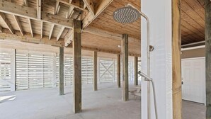 Una estança diàfana amb dutxa, bigues de fusta i una porta blanca.