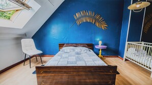 A bedroom with a sloped ceiling, a bed, a chair, a small table, a crib, and a decorative wall piece. - Farmhouse Vacation Rental for 15 People Near the Somme Bay (Friville-Escarbotin)