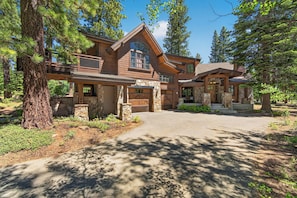 A large, two-story log cabin with a stone foundation, a front porch, and a garage. - Monthly Lease - Signature Lodge at Martis Camp by Tahoe Getaways - 4BR Estate! (Truckee)