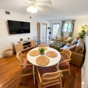 Ein modernes Wohnzimmer mit Flachbildfernseher, Esstisch mit gewobenen Unterlagen, Korbstühle, braunes Sofa und Deckenventilator.