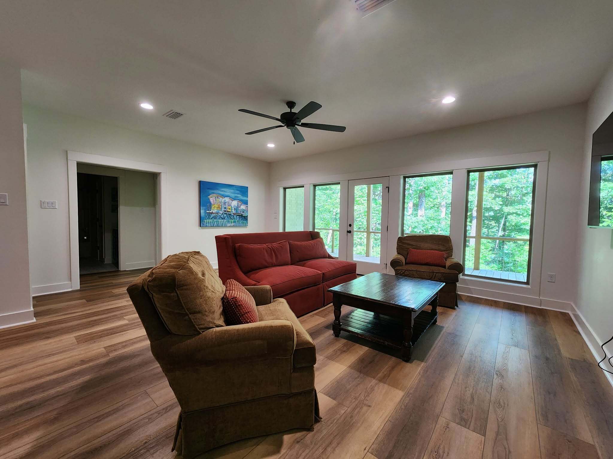 Un salon spacieux doté d’un plancher en bois, d’un canapé rouge, d’un fauteuil marron, d’une table basse et d’un ventilateur de plafond.