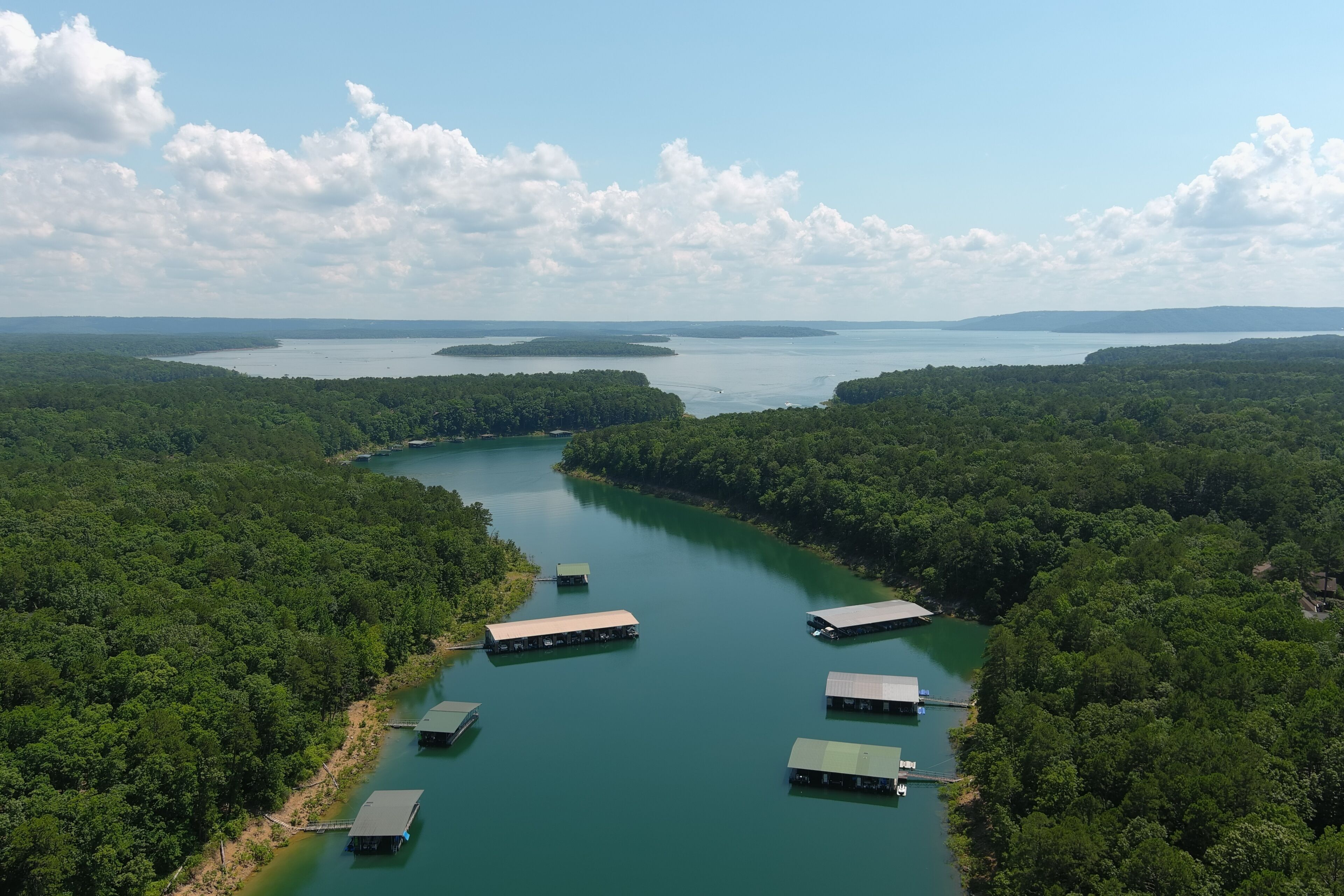 Une vue aérienne d’une rivière parsemée de structures flottantes, entourée d’une forêt dense.