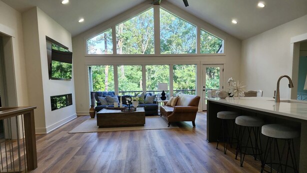 Un vaste espace de vie doté d’un haut plafond, de grandes fenêtres, d’un plancher en bois, d’un canapé, d’une table basse et d’un coin cuisine avec un tabouret de bar.