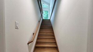 Un escalier en bois, doté d’une rampe, mène à une porte qui donne sur un paysage verdoyant.