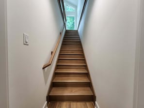 Eine Holztreppe mit Handlauf, die zu einer Tür mit Blick auf Grünanlagen führt.