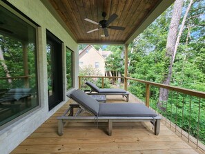 A wooden deck with two lounge chairs, a ceiling fan, and a view of a house and trees. - Brand New Family Lake Retreat with Two Living Areas (Greers Ferry)