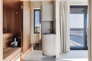 Ein modernes Badezimmer mit einer Holzsauna, einem Waschbecken und Blick ins Freie.