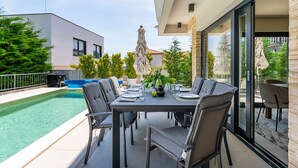 An outdoor dining area with a pool, modern chairs, and a table set for four. - Villa Tamaris Zadarvillas (Bibinje)