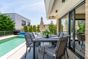 Ein Essbereich im Freien mit Pool, modernen Stühlen und einem Tisch für vier Personen.
