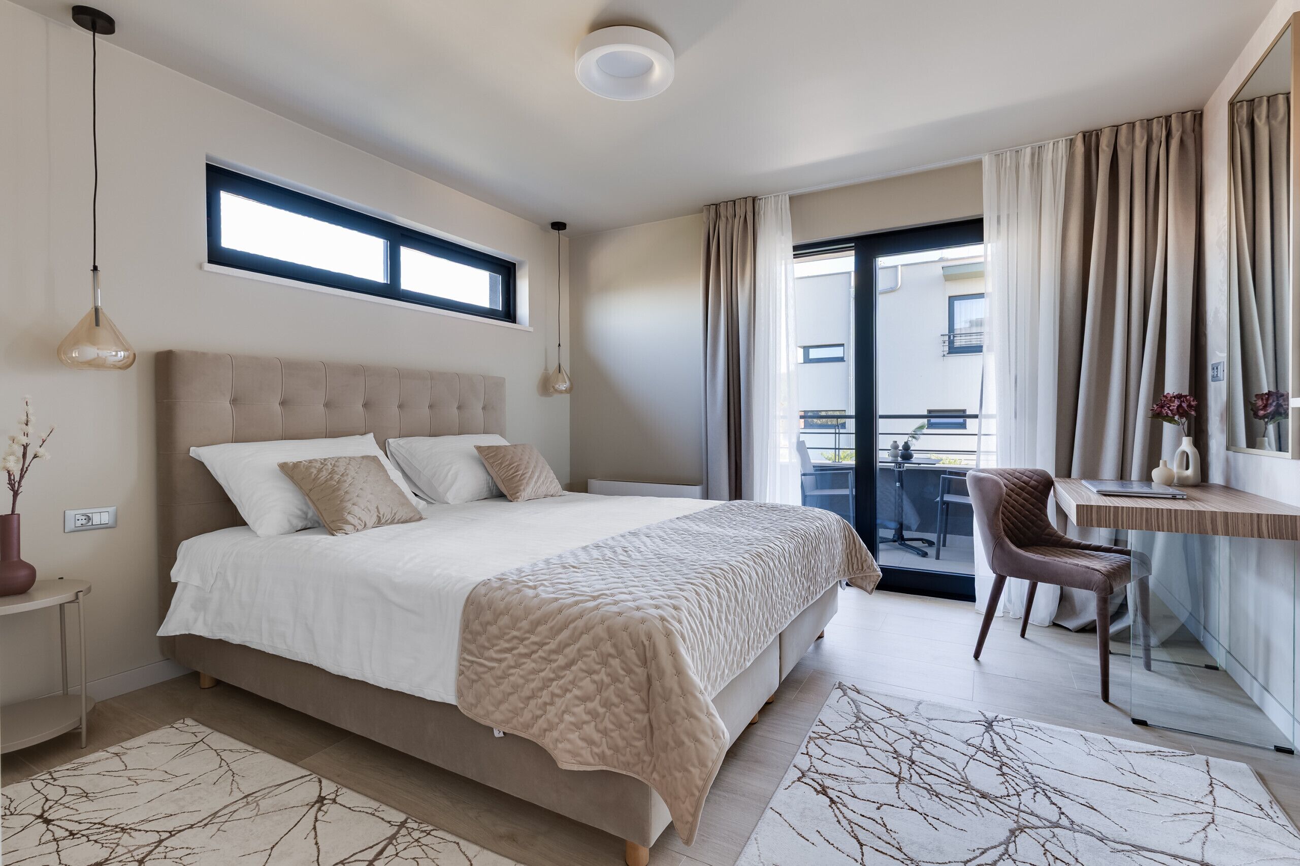 Ein modernes Schlafzimmer mit einem großen Bett, einem Schreibtisch, einem Stuhl, einem Fenster und einem Balkon.