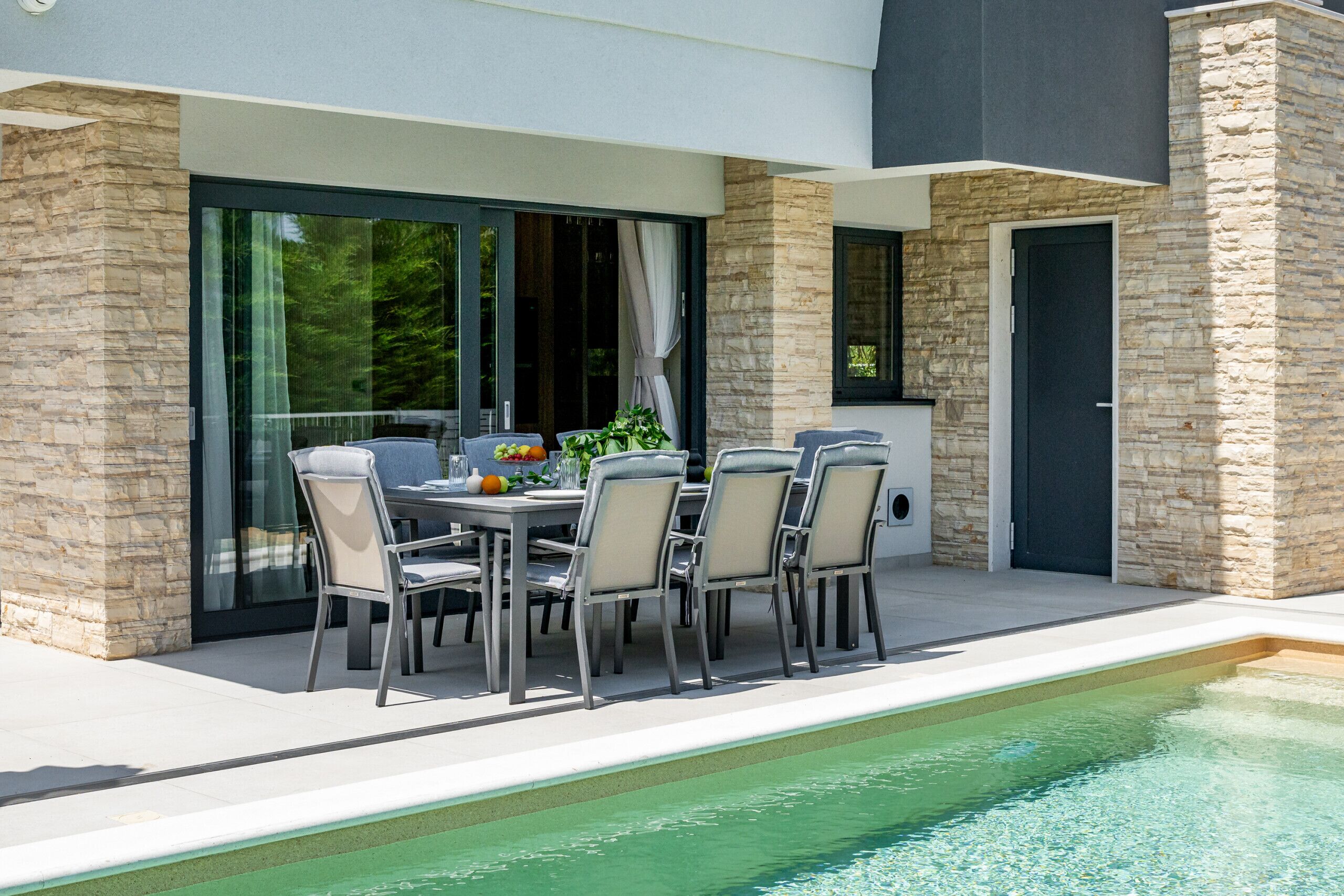 Ein moderner Außenbereich zum Essen mit Pool, Steinmauern und großen Fenstern.