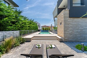 Ein moderner Poolbereich im Freien mit Liegestühlen und einer Steinmauer.