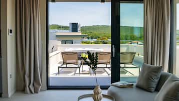 A modern room with a sofa, a small table with a vase, and a view of a balcony with chairs and a table.