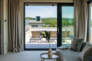 Ein modernes Zimmer mit einer Couch, einem kleinen Tisch mit einer Vase und Blick auf einen Balkon mit Stühlen und Tisch.