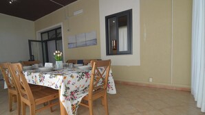 Een eetruimte met een tafel voor vier personen, houten stoelen, een vaas met bloemen en een raam met gordijnen.