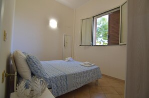 Un dormitorio con cama, ventana, puerta y una lámpara fijada a la pared.