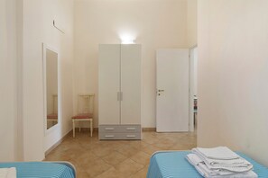 Ein Schlafzimmer mit Kleiderschrank, einem Sessel, einem Bett mit gestreifter Bettdecke und einer Tür zu einem anderen Raum.
