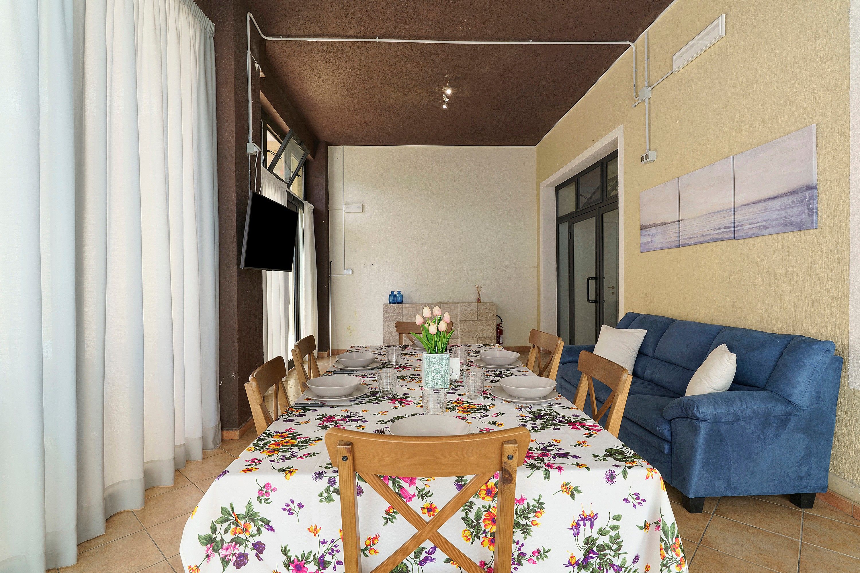 A dining area with a table set for four, chairs, a blue sofa, and a wall-mounted TV.