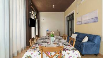A dining area with a table set for four, chairs, a blue sofa, and a wall-mounted TV.