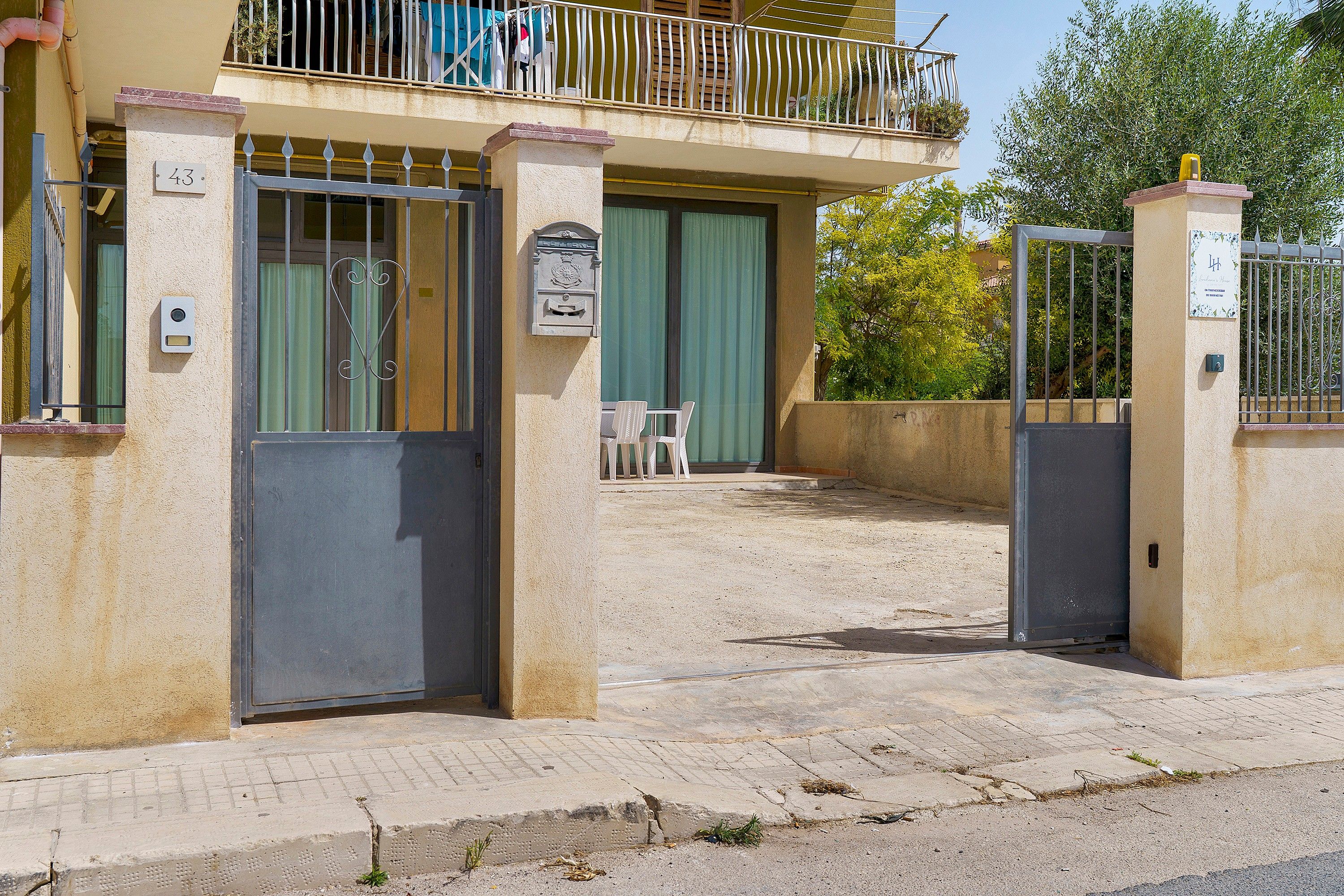 Une entrée fermée par un portail menant à un immeuble, avec une boîte aux lettres et une plaque d’immatriculation.