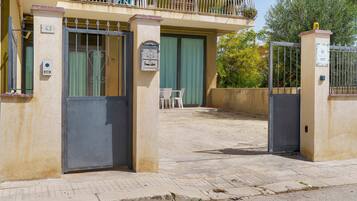 Une entrée fermée par un portail menant à un immeuble, avec une boîte aux lettres et une plaque d’immatriculation.