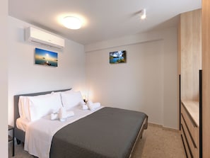 Ein Hotelzimmer mit einem Bett, einer Wand-Klimaanlage, zwei gerahmten Bildern und einem Holzkasten.
