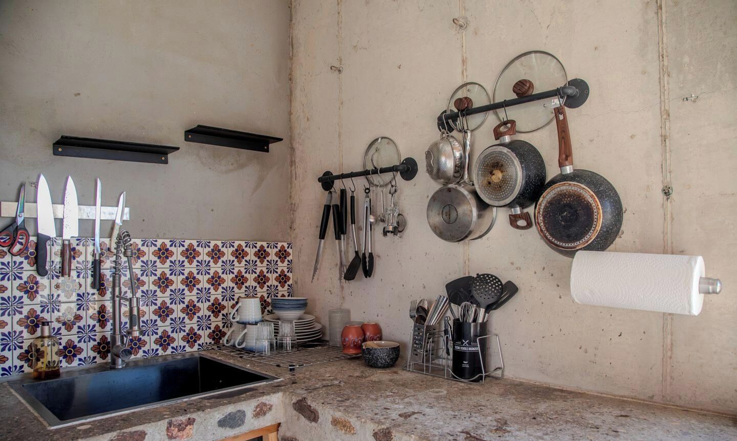 A kitchen with a sink, tiled backsplash, hanging pots, and utensils.