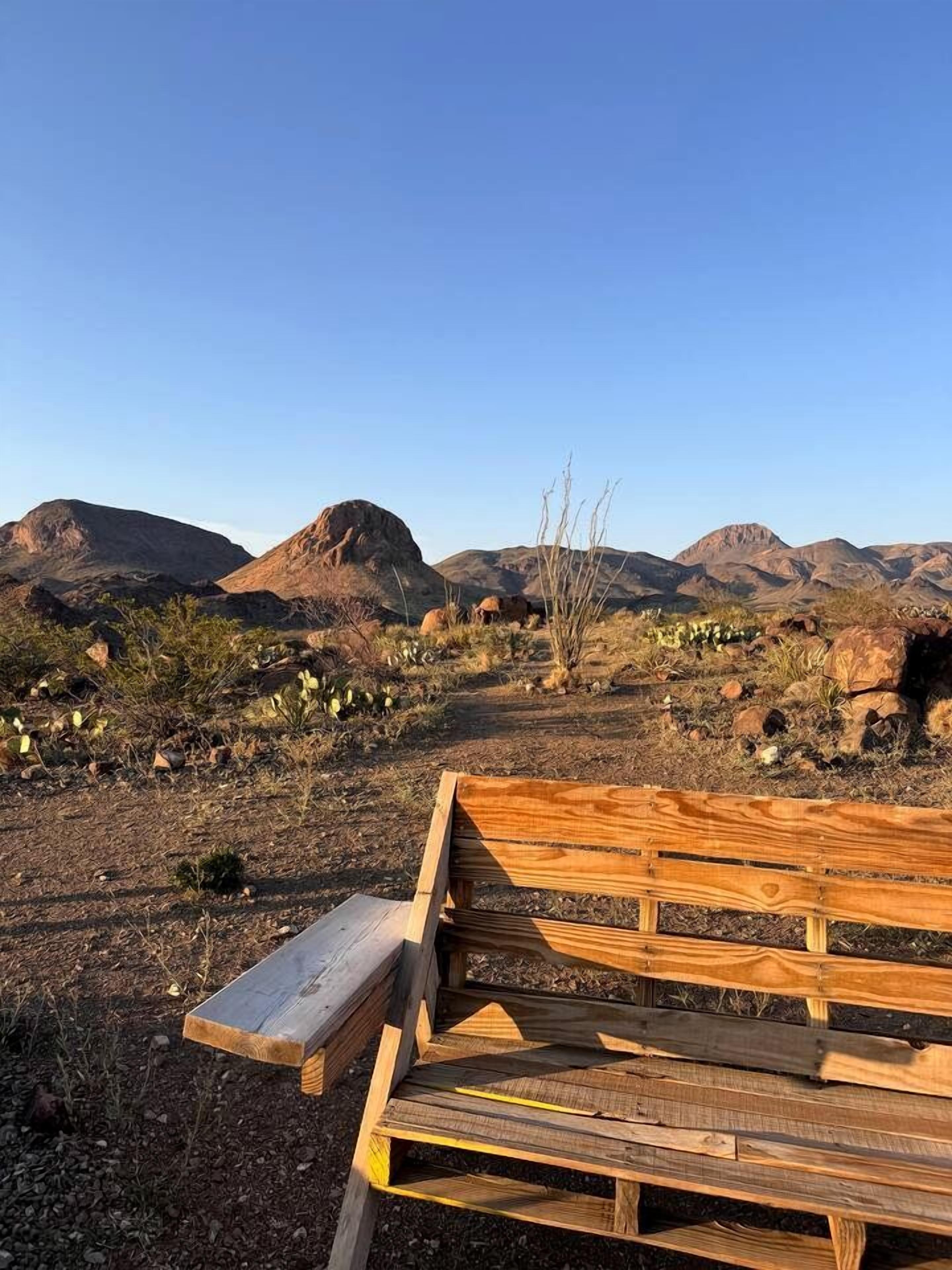 A wooden bench in a desert landscape with mountains in the background.