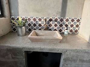 Ein Steinwaschbecken mit Metallbecken, ein Topfpflanze und eine Handseifenflasche auf einer Arbeitsplatte.