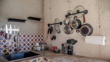 A kitchen with a tiled backsplash, a sink, and various utensils and cookware hanging on the wall.