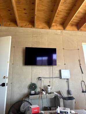 Ein Zimmer mit einem an der Wand befestigten Flachbildfernseher, Steckdosen, einem Ventilator und einer Mülleimer.