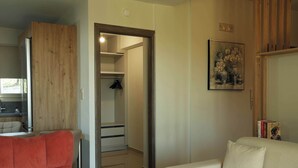 A room with a wooden wardrobe, a white sofa, a framed picture on the wall, and a door leading to a bathroom. - Olive & Raki Luxury Pool Villa, Crete Garden Oasis (Agioi Theodoroi)