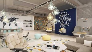 Un moderno espacio de lounge con asientos, un mapa del mundo y un letrero que dice 'Work Hard, Play Hard'.