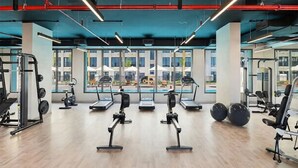 Un gimnasio moderno con máquinas de cardio, pesas libres y vistas a una piscina y edificios.